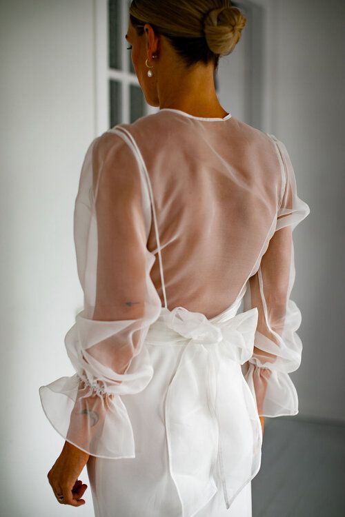 a plain wedding dress with spaghetti straps, an open back and a sheer wrap dress topper with long sleeves are a lovely combo for a modern bride