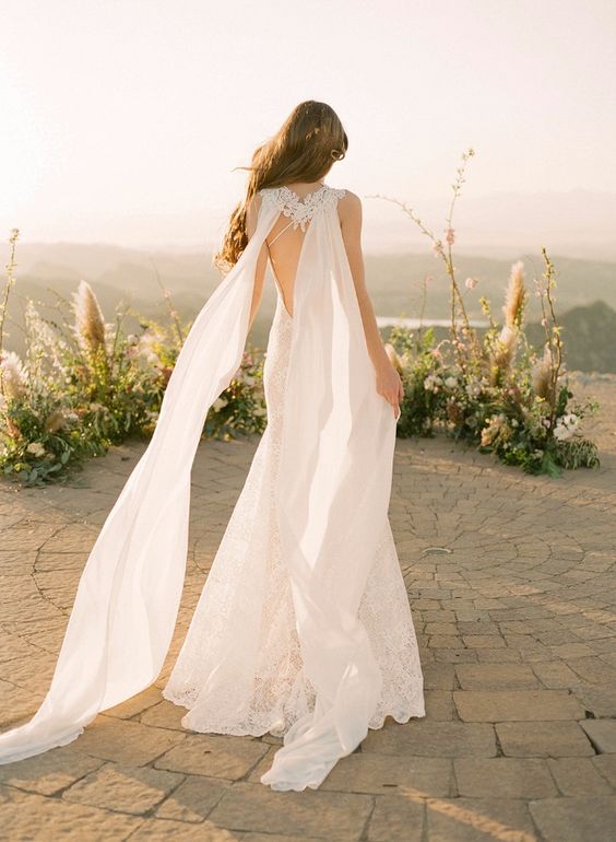 a romantic lace mermaid wedding dress with a cutout lace back and a matching sheer cape veil is wow