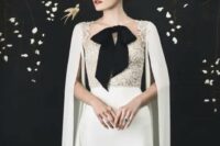 an elegant neutral wedding dress with a lace bodice, a plain skirt, a capelet, a black bow on the front for a refine dlook