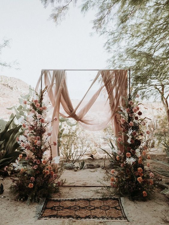 a beautiful and breezy wedding backdrop with blush drapes, pink and white blooms and branches on both sides of the arch