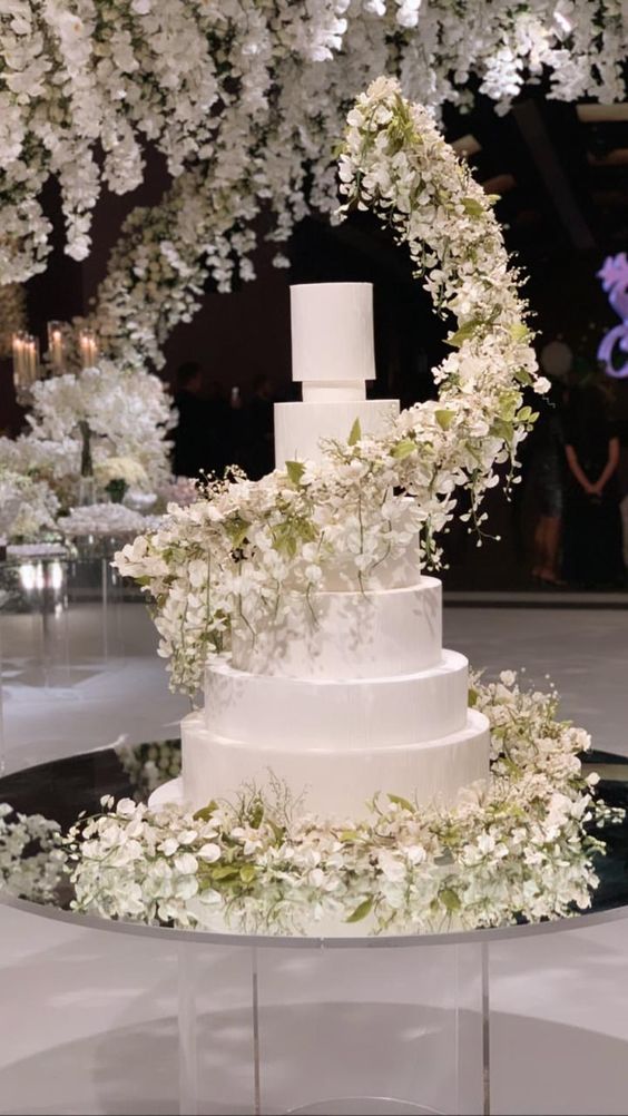 a beautiful formal white wedding cake with a large and lush white flower and green swirl around is a very exquisite idea
