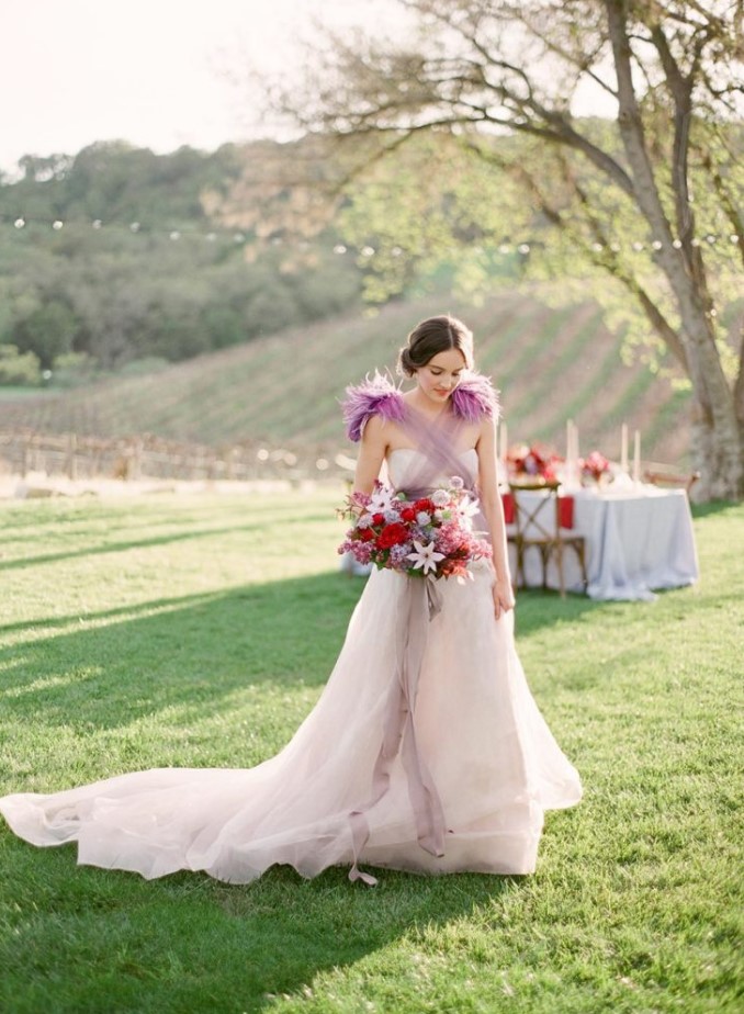 a blush A line wedding dress with a train and a fuchsia shoulder accent of wispy feathers create a lovely bridal look