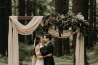 03 a beautiful and refined wedding arch with neutral drapes, greenery and dark blooms plus a boho rug is a stylish idea for a wedding