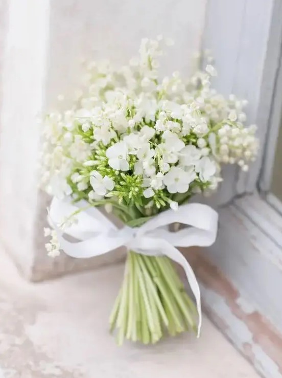 a beautiful and romantic white wedding bouquet of lily of the valley and large blooms with a ribbon bow is amazing