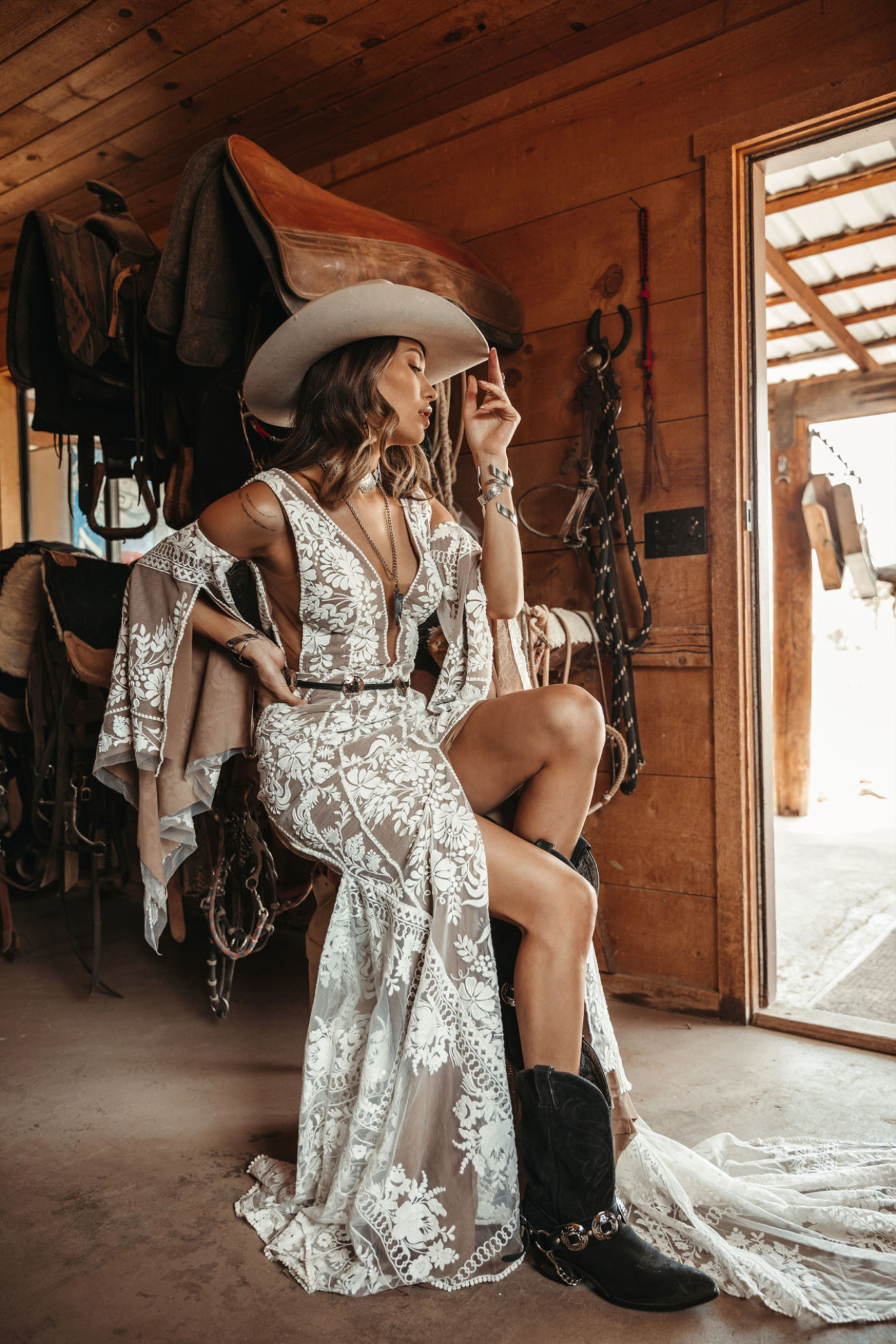 a beautiful nude and white lace A line wedding dress with a covered plunging neckline and bell sleeves, black boots, a neutral hat and statement accessories