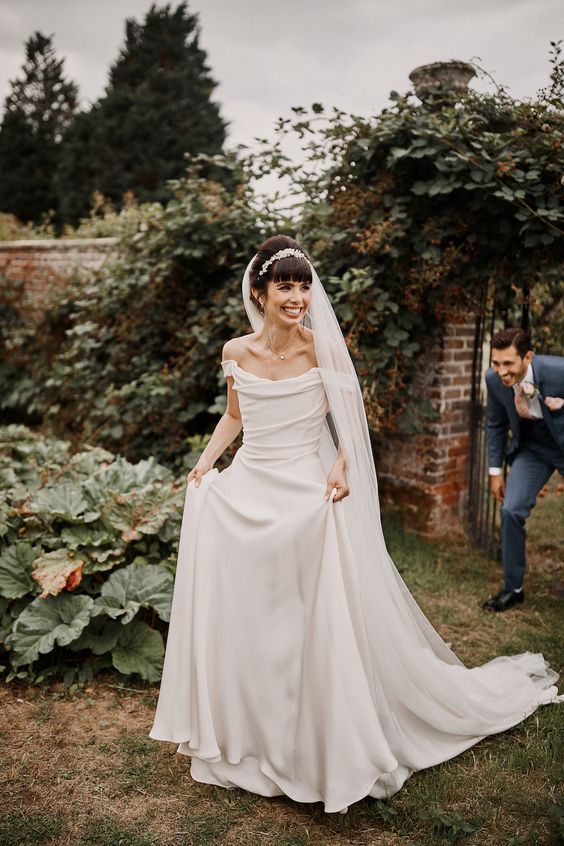 a beautiful off the shoulder A-line wedding dress with a draped bodice and a plain skirt with a train is a lovely idea for a wedding