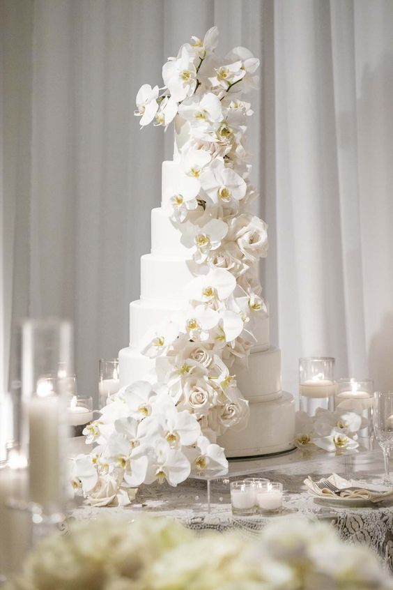a chic and refined white wedding cake with white orchid and rose swirls is a very stylish idea for a formal wedding