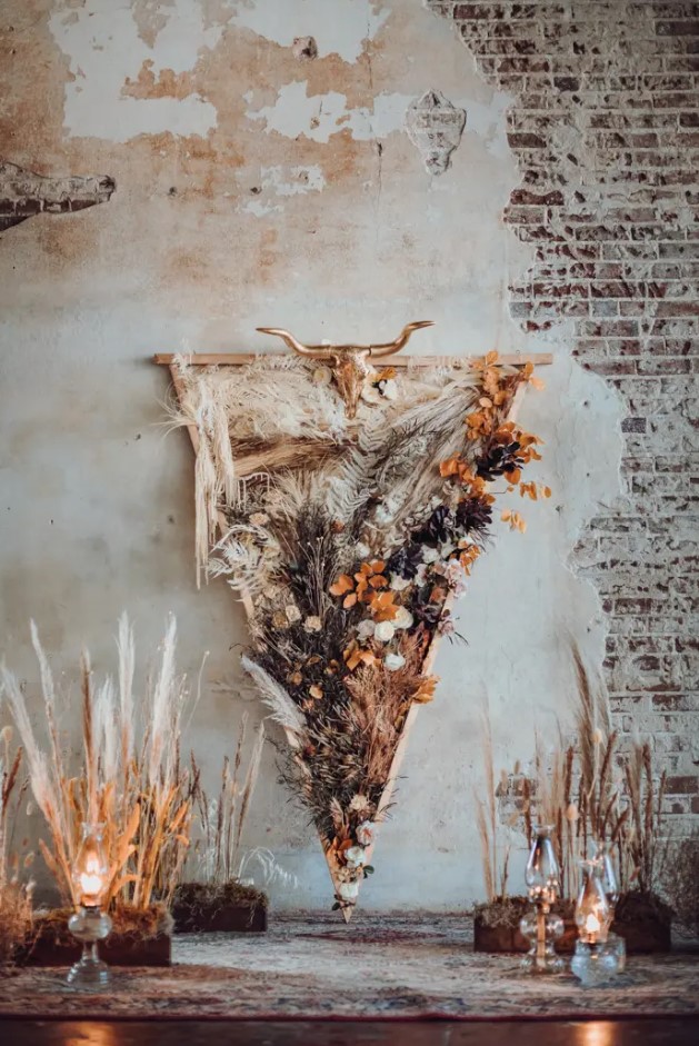 a bold western wedding backdrop of a triangle with bold and dried blooms and leaves, a gilded skull, some grasses along the aisle