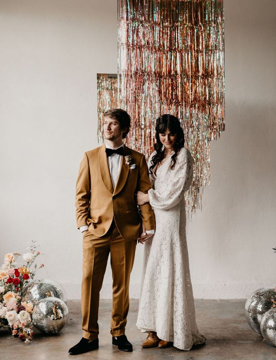 a chic disco-themed wedding backdrop of tinsel fringe, disco balls and neutral and bold blooms is amazing