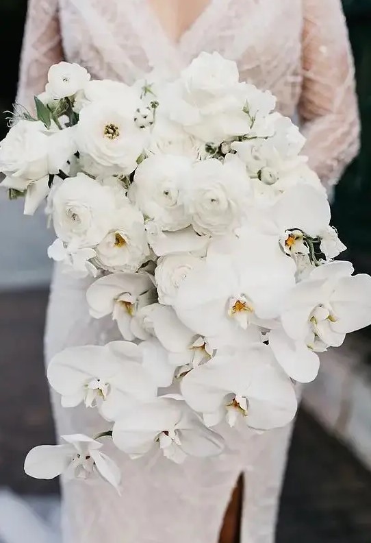 a cascading white wedding bouquet composed of ranunculus and orchids looks very sophisticated