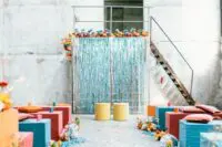 08 a colorful wedding ceremony space with a turquoise tinsel wedding backdrop, colorful poufs and stools and bright blooms