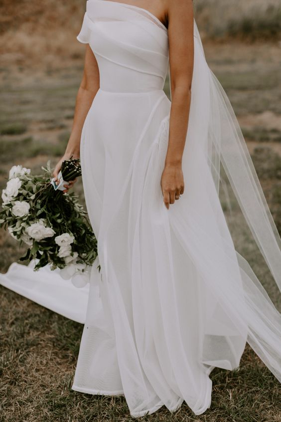 a dreamy one shoulder wedding dress with a draped bodice and a pleated skirt with a train is a lovely and chic idea for a wedding