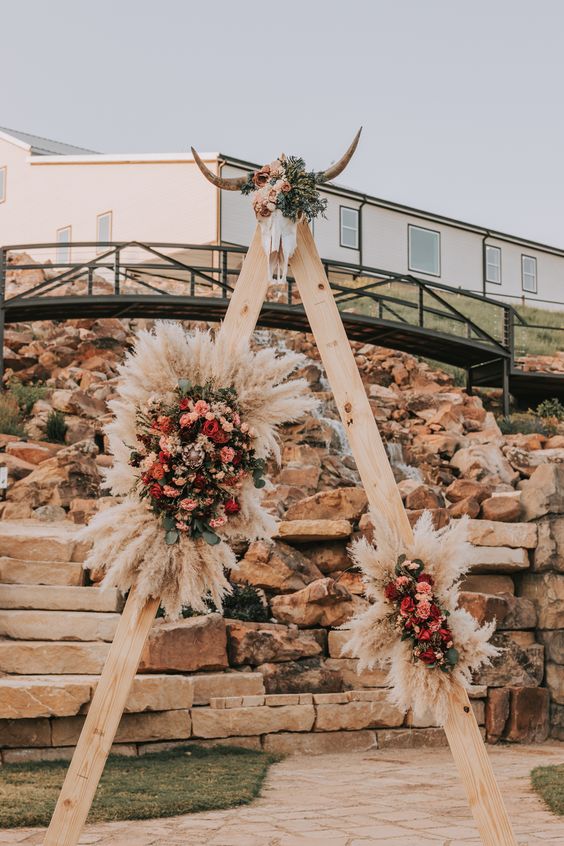 a western wedding arch with bright blooms, greenery and pampas grass, with a skull decorated with blooms on top
