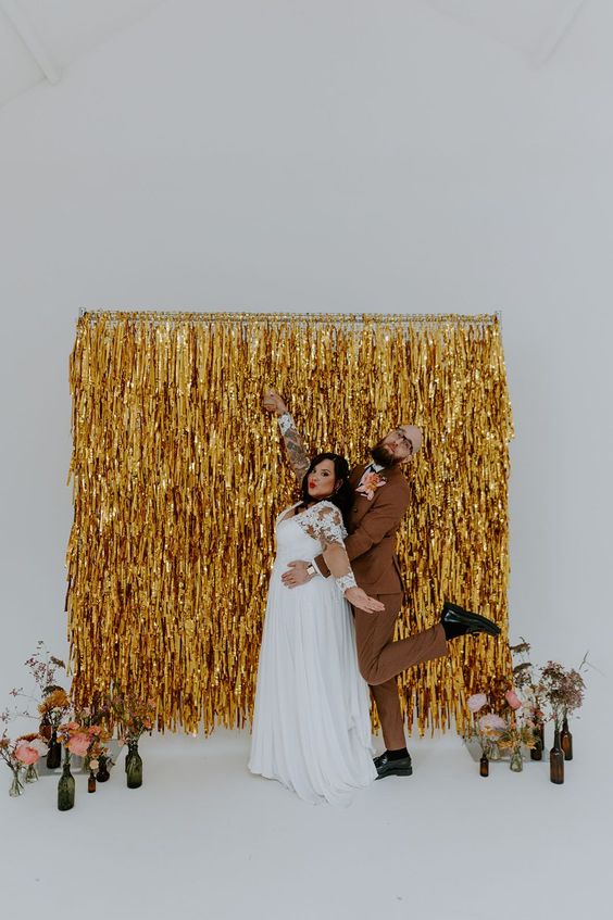 a fun modern wedding backdrop of gold tinsel streamers and some blooms in bottles is a cool piece to DIY