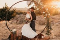 10 a western wedding arch with greenery, white and orange blooms, a cowhide rug, tree stumps is a perfect idea for a boho ceremony