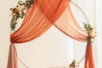 11 a bright wedding backdrop of a large hoop, orange drapes, neutral and orange blooms, candles and candle lanterns around