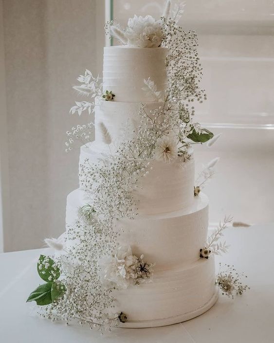 a white textural wedding cake with a baby's breath swirl, white blooms, dried grasses and greenery is a very chic and stylish idea