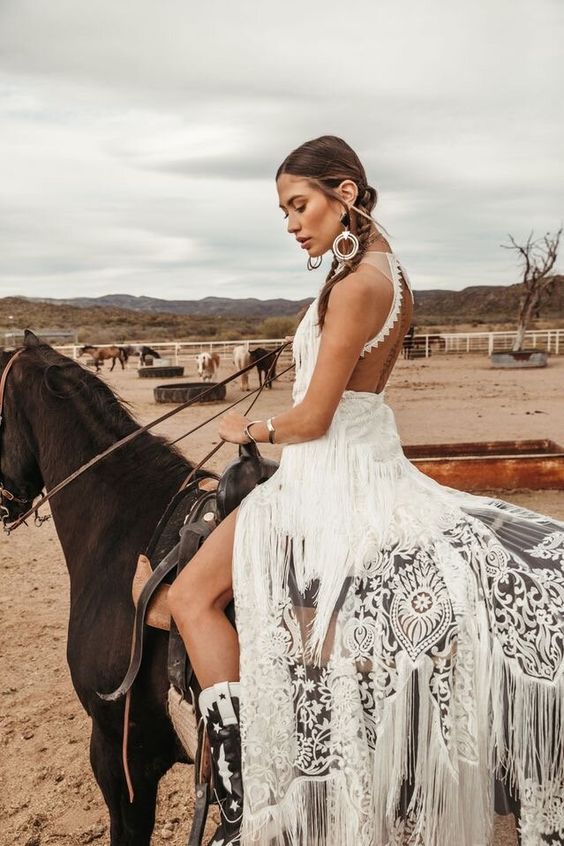a fabulous western bridal look with a lace applique halter neckline wedding dress, with an open back and long fringe plus black and white boots and statement jewelry
