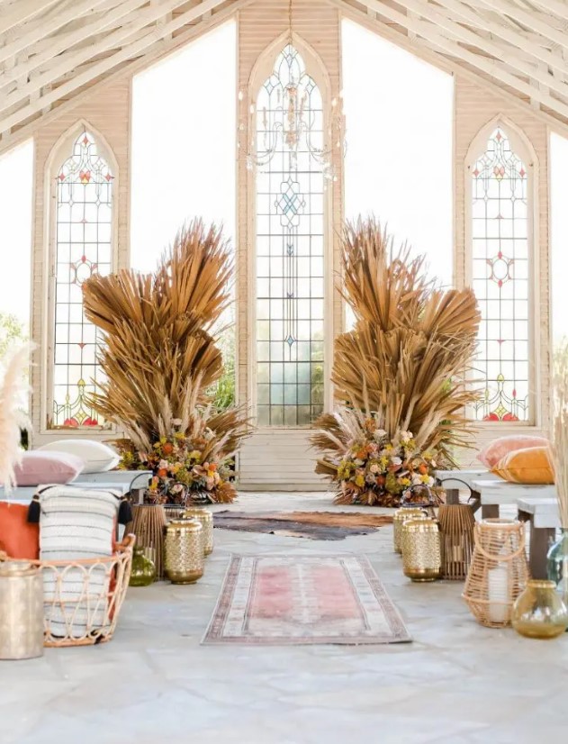 a western wedding ceremony space with fronds and dried grasses plus bold blooms, rugs and gilded and wooden lanterns