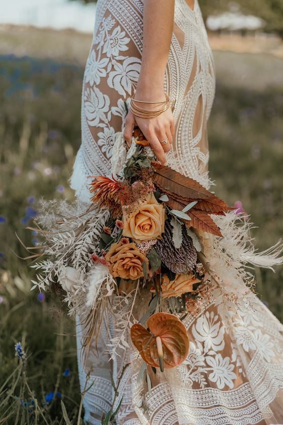 a beautiful boho western wedding bouquet of orange and rust bouquets, greenery, white roses adn dried leaves is a bold and catchy idea