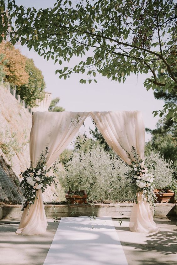 a classic wedding backdrop of neutral drapes, white blooms and greenery is a lovely idea for many wedding styles
