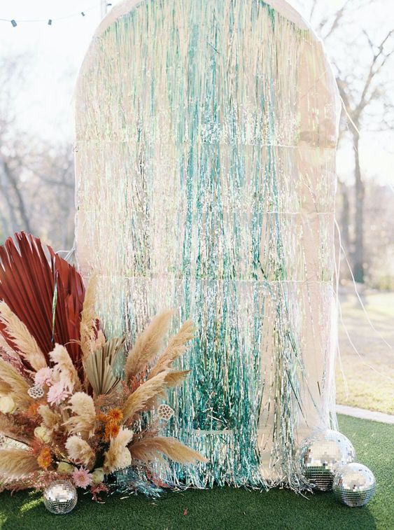 a lovely wedding backdrop of silver and turquoise tinsel fringe and a pink and rust floral arrangement with fronds