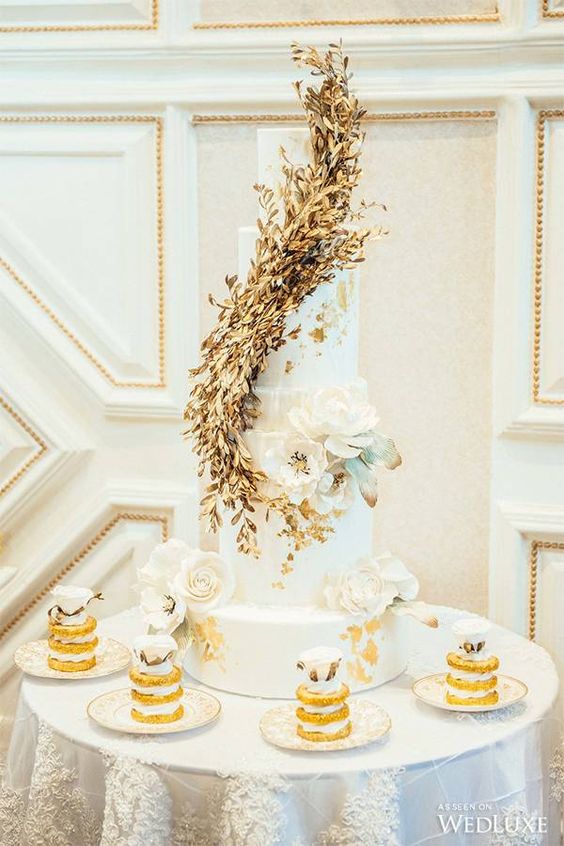 a white wedding cake with gold foil, with a gold leaf swirl and white sugar and fresh blooms i s a refined idea for a wedding