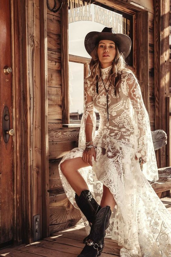 a gorgeous western bridal look with a lace applique A-line wedding dress with a turtleneck, bell sleeves, black cowboy boots and a brown hat