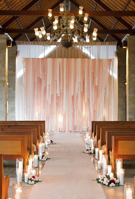 a simple and cool wedding ceremony space with a blush and creamy streamer wedding backdrop, pillar candles and blooms is wow