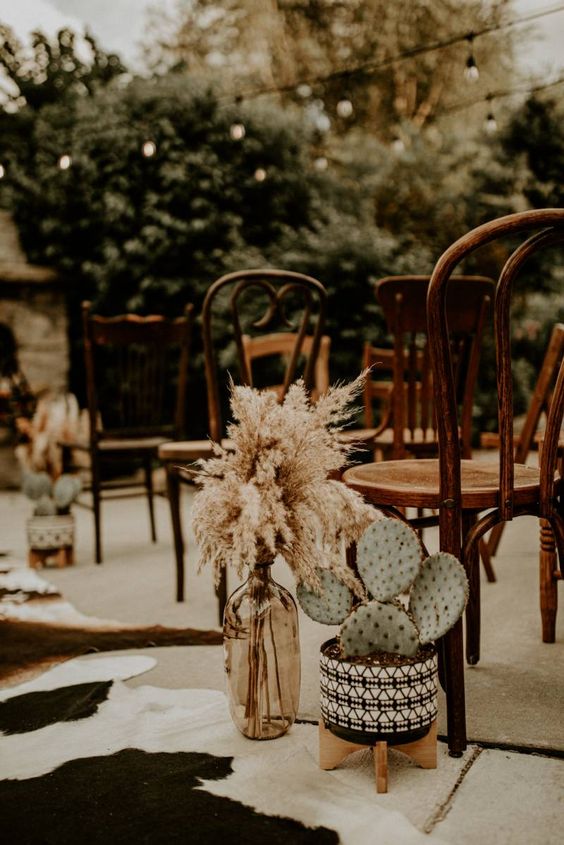 a bold western wedding aisle with cowhide rugs, potted cacti and pampas grass in a bottle plus mismatching chairs