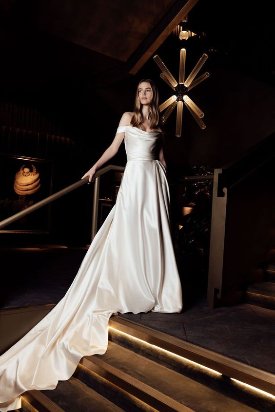 a modern off the shoulder wedding ballgown with a draped neckline and a draped skirt with a long train is refined and chic