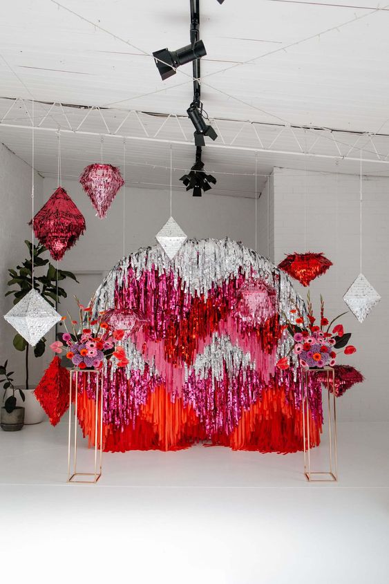 a super bold wedding backdrop of silver, pink and red tinsel streamers and matching colorful blooms and pinatas