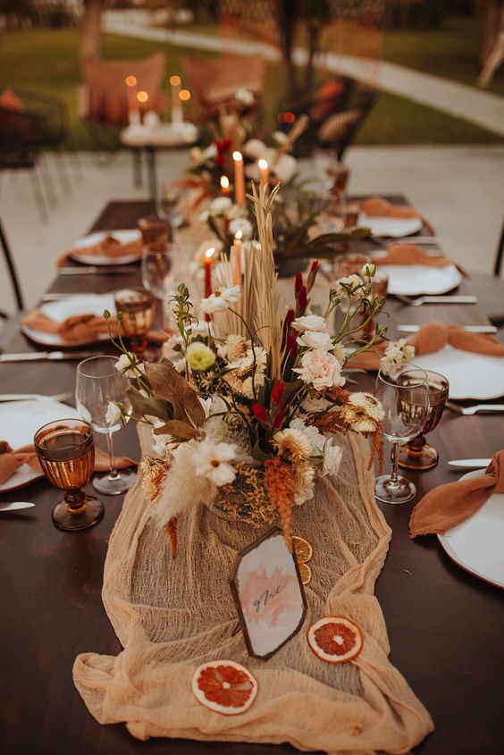a bold western wedding table setting with an orange runner and rust napkins and glasses, bold dried blooms and grasses