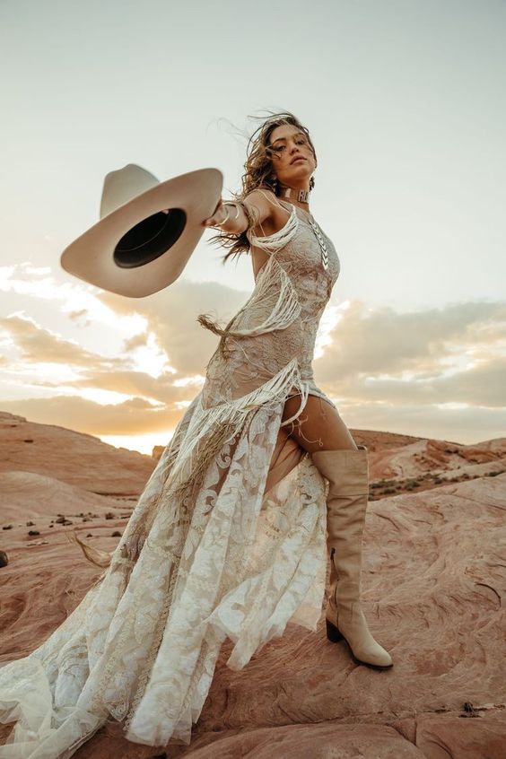 a nude halter neckline lace wedding dress, tall tan boots, statement accessories and a creamy hat for creating a western bridal look