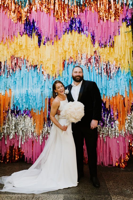 a super colorful and tinsel streamer wedding backdrop is a gorgeous idea for a fun and maybe disco-themed wedding