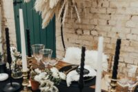 18 a bold western wedding tablescape with a black runner and black and white candles, black placemats and gilded touches plus pampas grass over the space