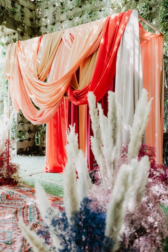 a gorgeous colorful wedding backdrop of bright drapes, pampas grass and dried blooms in various colors is wow