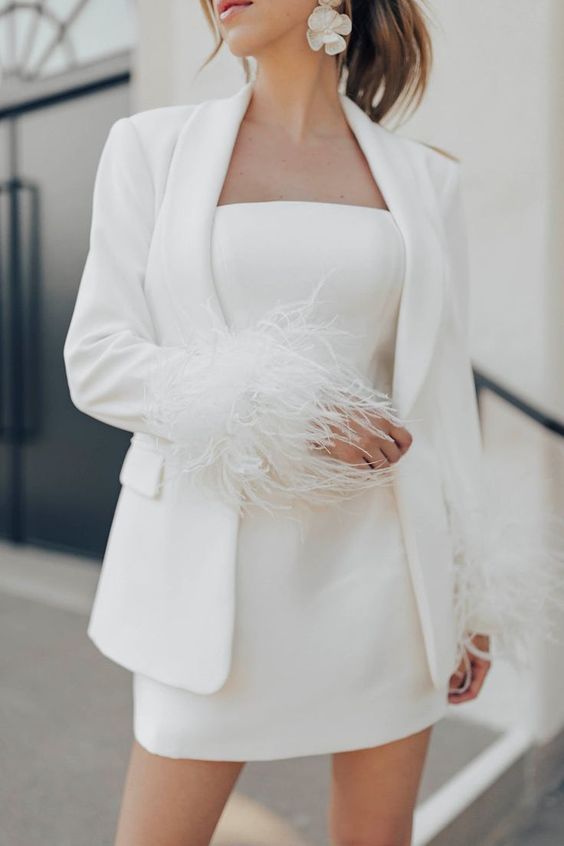 a minimalist bridal ensemble with a plain strapless mini wedding dress, a matching blazer with feather sleeves