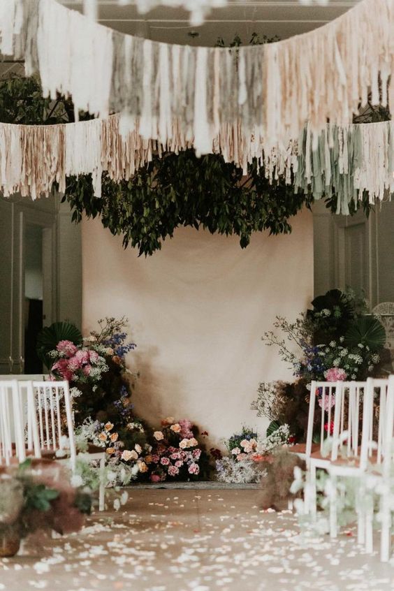 a beautiful wedding ceremony space done with pink and white blooms and greenery, neutral and gold streamers over the space and petals on the floor