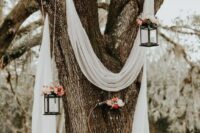 19 a living tree wedding backdrop of a white drape, bold blooms on candle lanterns and embroidery hoop is a chic idea