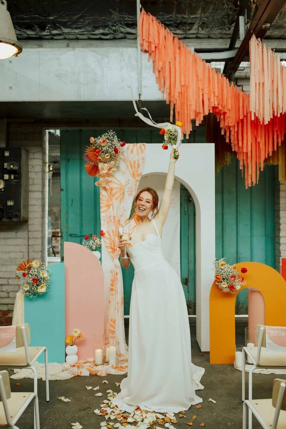 a colorful and artful wedding backdrop with orange, blue and pink pieces, colorful streamers, blooms and candles is amazing