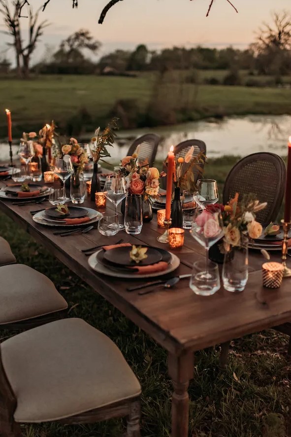 a bright western wedding tablescape with bright blooms and dried grasses, orange candles, black and grey plates and smaller candles