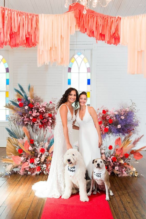 a colorful wedding ceremony space with bright blooms, a red carpet and blush and coral streamers over the space