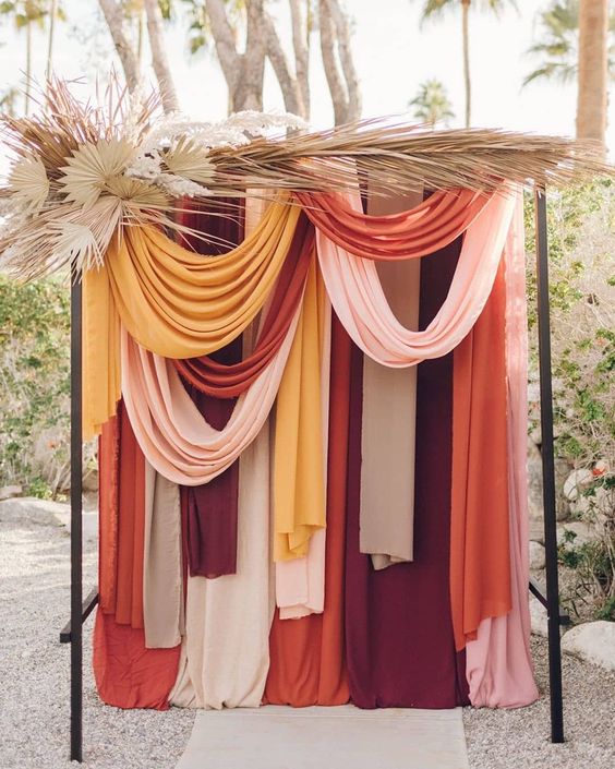a modern colorful drape wedding backdrop with pampas grass and fronds is a bold idea for a modern boho wedding