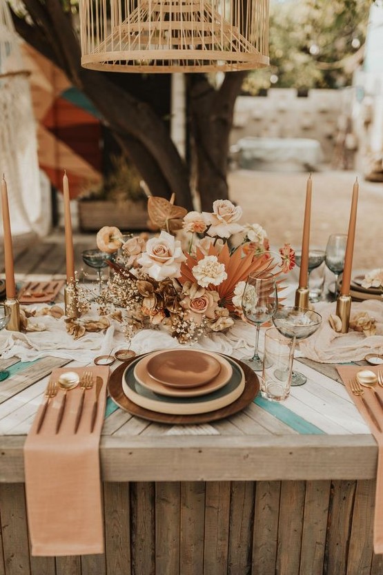 a chic wedding tablescape with layered plates, a lush blush and rust floral centerpiece, rust candles and rust napkins