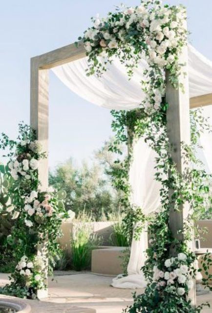a neutral wedding arbor with greenery, white blooms and drapes is a very chic and beautiful idea for a wedding