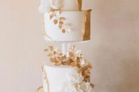 23 a white and gold wedding cake with a clear stand in the center, with sugar blooms and leaves and gold leaf swirls around it
