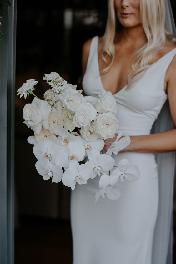 a simple and modern white wedding bouquet of orchids and roses is a stylish idea for an all-white wedding