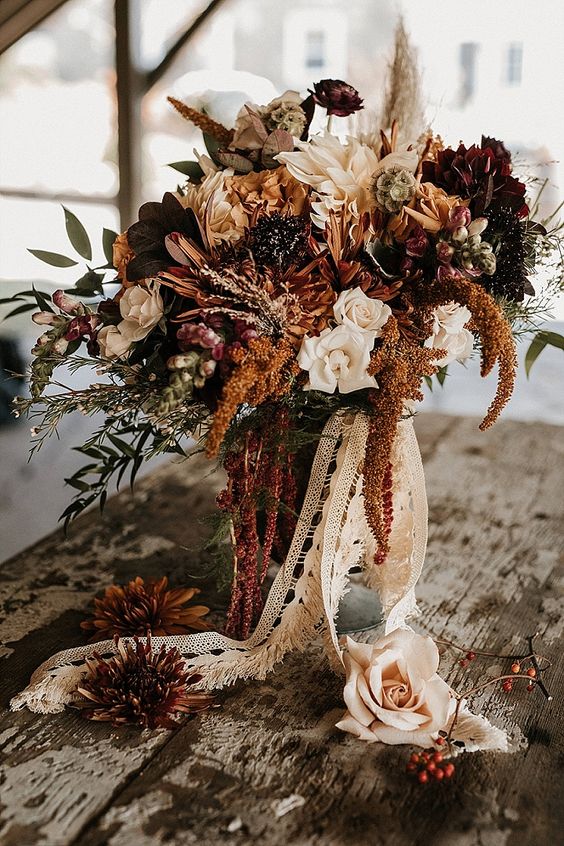 a western wedding bouquet of neutrla, burgundy and rust blooms, greenery and long lace ribbon is amazing for a western bride