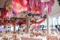 26 a bright modern wedidng reception space with blush tables and blooms, pink and blush balloons and colorful tinsel fringe